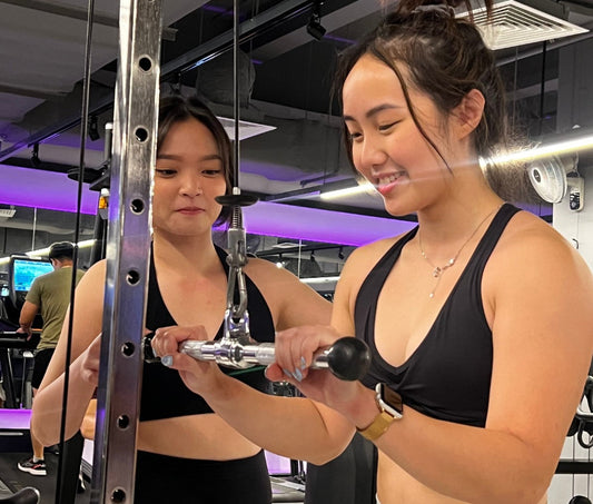 AlmightyPT female personal trainer coaching a woman through a cable strength training exercise in a Singapore gym
